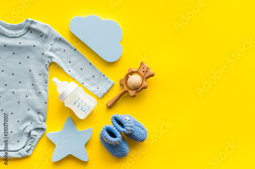Baby background - blue color. Clothes and accessories for newborn boy on yellow table top-down frame copy space