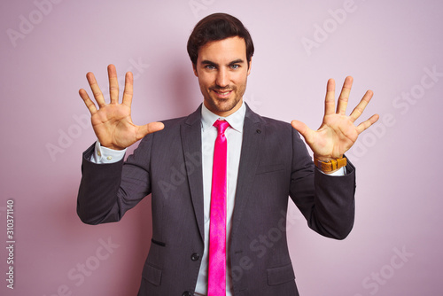 Young handsome businessman wearing suit and tie standing over isolated pink background showing and pointing up with fingers number ten while smiling confident and happy.