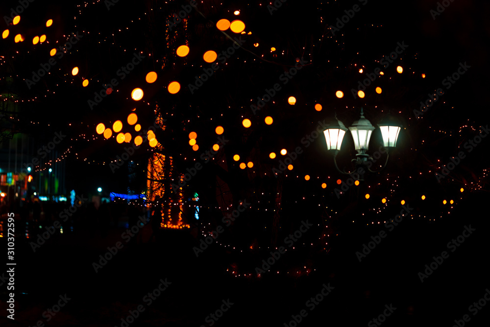 Colorful lights on the trees and retro lanterns at  illuminated city street, unfocused background of night city with Christmas illuminations.