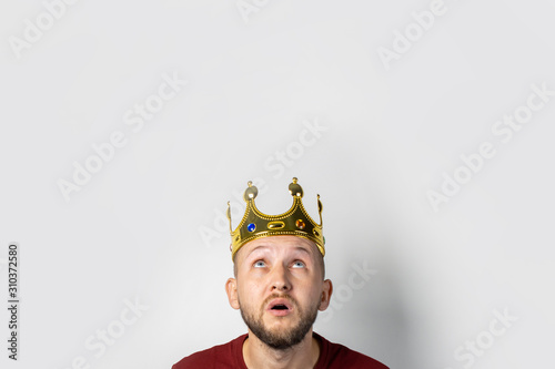 Young man with a crown on his head on a light background. Concept is king, luck, gain, rich, dream, goal, aspiration. Banner © Alex