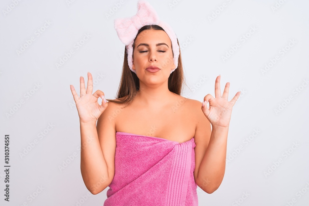Beautiful young woman wearing pink shower towel and beauty headband over white background relax and smiling with eyes closed doing meditation gesture with fingers. Yoga concept. Beautiful young woman wearing pink shower towel and beauty headband over white background relax and smiling with eyes closed doing meditation gesture with fingers. Yoga concept.