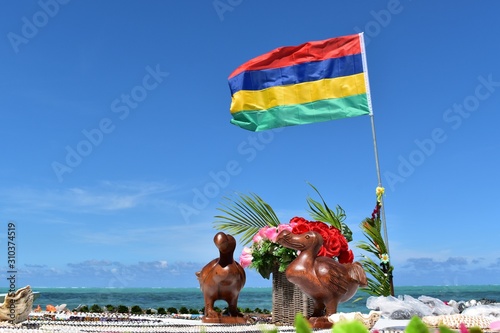 Picture of a wooden statue representing the symbol of Mauritius the Dodo bird. Mauritius flag in background.