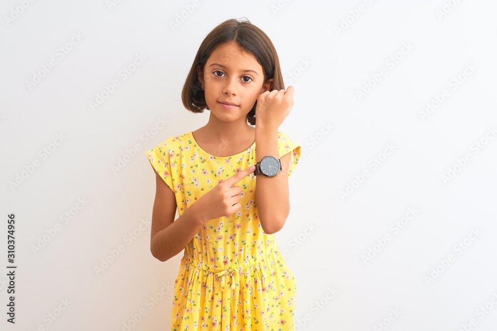 Young beautiful child girl wearing yellow floral dress standing over isolated white background In hurry pointing to watch time, impatience, looking at the camera with relaxed expression Young beautiful child girl wearing yellow floral dress standing over isolated white background In hurry pointing to watch time, impatience, looking at the camera with relaxed expression