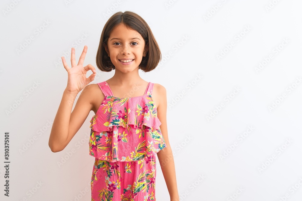 Young beautiful child girl wearing pink floral dress standing over isolated white background smiling positive doing ok sign with hand and fingers. Successful expression. Young beautiful child girl wearing pink floral dress standing over isolated white background smiling positive doing ok sign with hand and fingers. Successful expression.