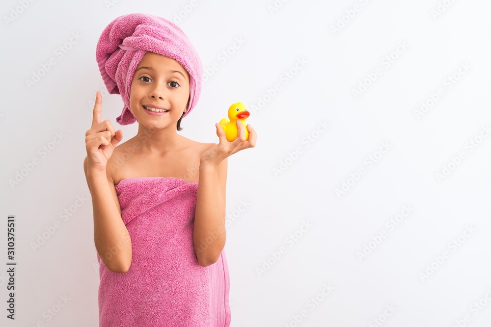 Beautiful child girl wearing shower towel holding duck over isolated white background surprised with an idea or question pointing finger with happy face, number one Beautiful child girl wearing shower towel holding duck over isolated white background surprised with an idea or question pointing finger with happy face, number one