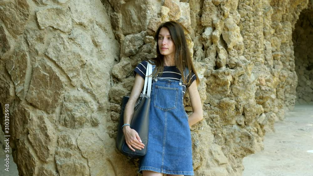 A beautiful woman standing at architectural column, looking around thoughtfully in Park Guell. Barcelona. Spain. 4K A beautiful woman standing at architectural column, looking around thoughtfully in Park Guell. Barcelona. Spain. 4K