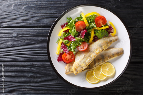 Fotografi Freshwater fish fillet of zander fried with fresh vegetables and lemon close-up in a plate