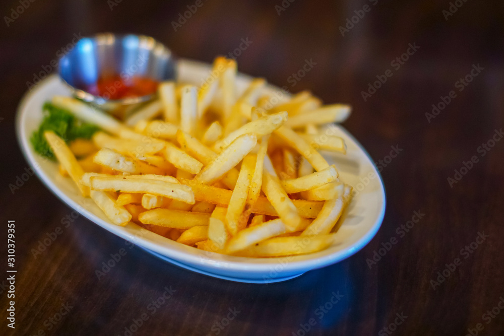 Serving of french fries with tomato sauce on white plate on dark wooden background Serving of french fries with tomato sauce on white plate on dark wooden background
