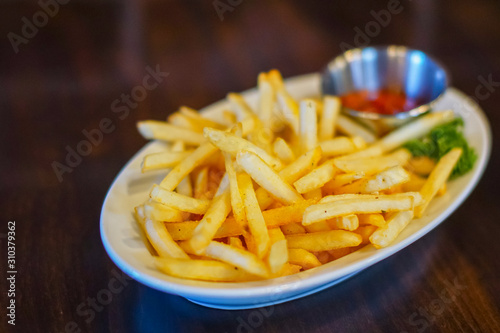 Serving of french fries with tomato sauce on white plate on dark wooden background