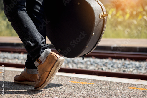 Close up leg of traveler with guitar case at railway station.