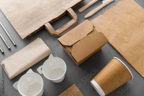 package, recycling and eating concept - disposable paper container for takeaway food with cups, bags, napkins and cutlery on table photo