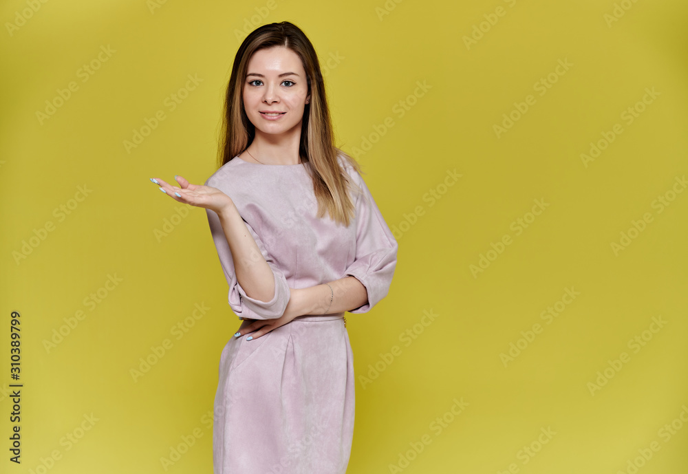 Portrait of a pretty young smiling woman on a yellow background in a pink dress with long straight hair. Standing right in front of the camera, Shows emotions, talks in different poses. Portrait of a pretty young smiling woman on a yellow background in a pink dress with long straight hair. Standing right in front of the camera, Shows emotions, talks in different poses.
