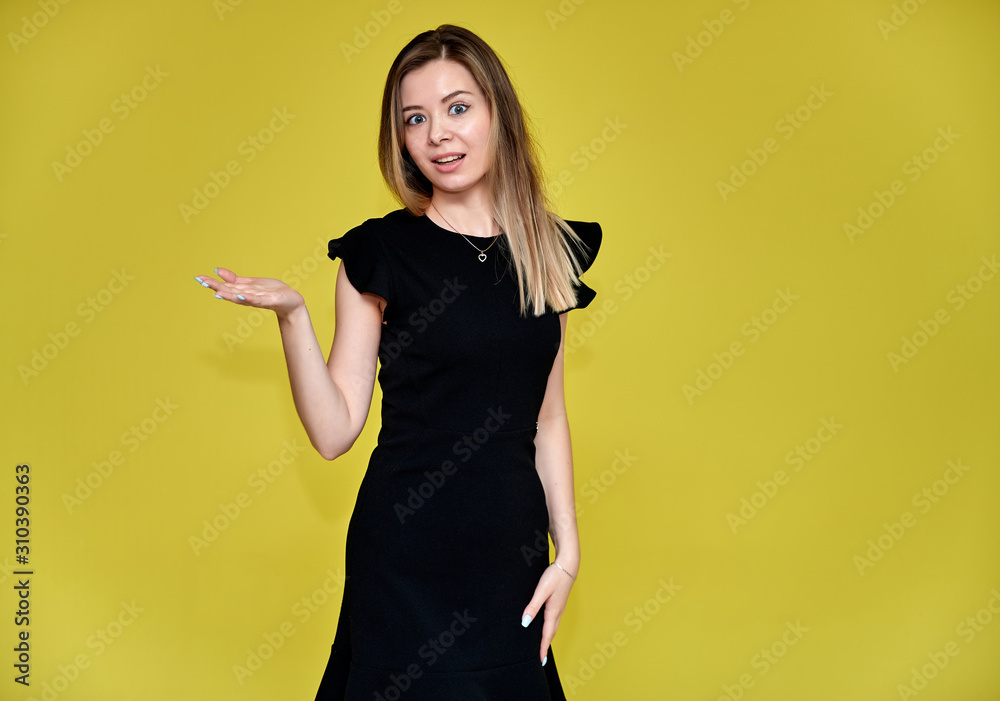 Portrait of a pretty young smiling woman on a yellow background in a black dress with long straight hair. Standing right in front of the camera, Shows emotions, talks in different poses. Portrait of a pretty young smiling woman on a yellow background in a black dress with long straight hair. Standing right in front of the camera, Shows emotions, talks in different poses.