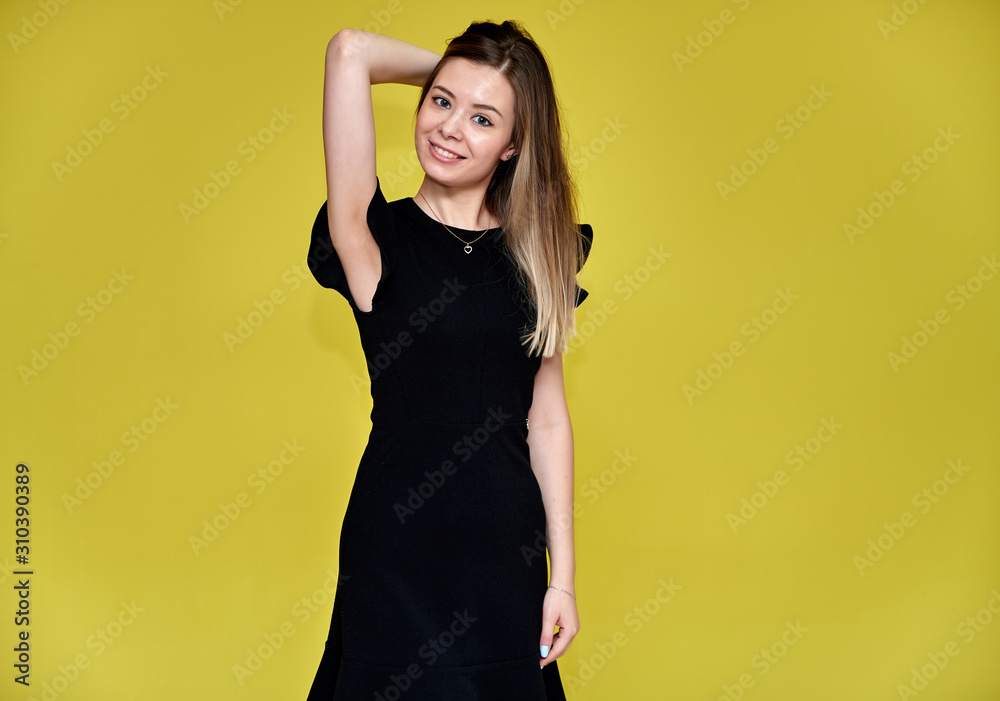 Portrait of a pretty young smiling woman on a yellow background in a black dress with long straight hair. Standing right in front of the camera, Shows emotions, talks in different poses. Portrait of a pretty young smiling woman on a yellow background in a black dress with long straight hair. Standing right in front of the camera, Shows emotions, talks in different poses.