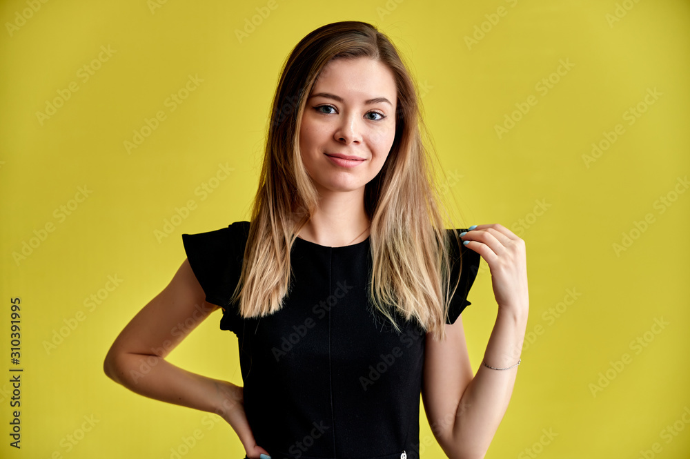 Close-up portrait of a pretty young smiling woman on a yellow background in a black dress with long straight hair. Standing right in front of the camera, Shows emotions, talks in different poses. Close-up portrait of a pretty young smiling woman on a yellow background in a black dress with long straight hair. Standing right in front of the camera, Shows emotions, talks in different poses.