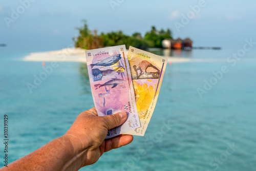 Fototapeta Naklejka Na Ścianę i Meble -  A tourist's show Maldivian rufiyaa bank note when she traveling in Maldives. Money of Maldives bank note in female's hand on the background of the island, salary incomes.
