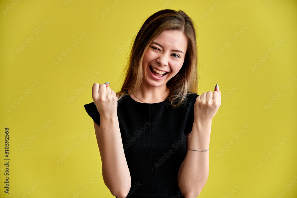 Close-up portrait of a pretty young smiling woman on a yellow background in a black dress with long straight hair. Standing right in front of the camera, Shows emotions, talks in different poses. Close-up portrait of a pretty young smiling woman on a yellow background in a black dress with long straight hair. Standing right in front of the camera, Shows emotions, talks in different poses.