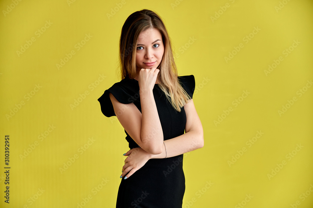 Portrait of a pretty young smiling girl on a yellow background in a black dress with long straight hair. Standing right in front of the camera, Shows emotions, talks in different poses. Portrait of a pretty young smiling girl on a yellow background in a black dress with long straight hair. Standing right in front of the camera, Shows emotions, talks in different poses.