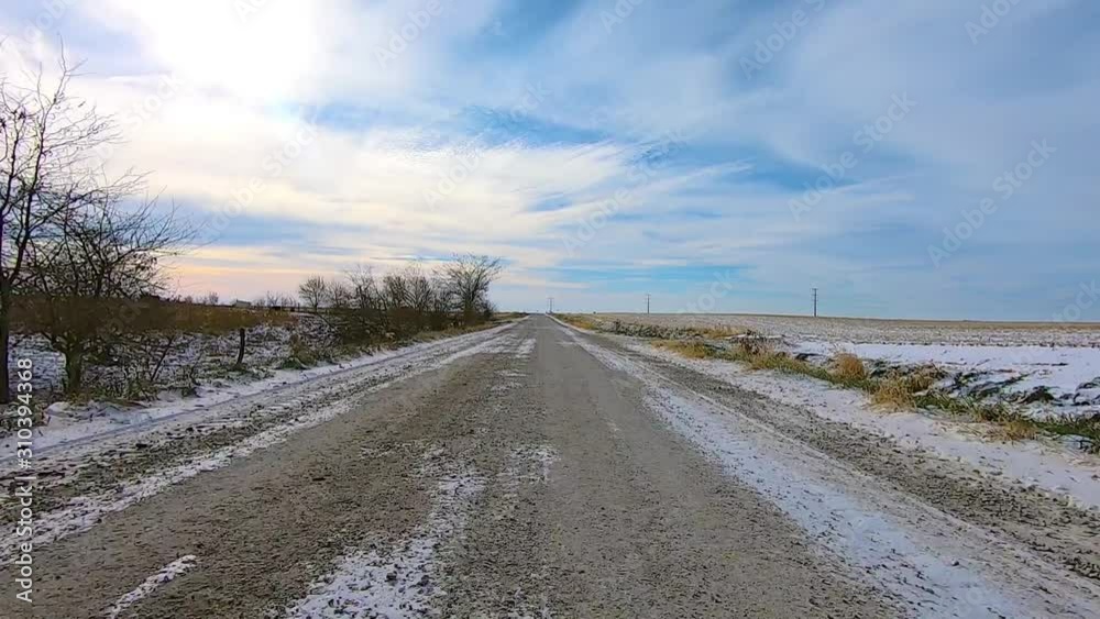 2X, POV through the rear window while driving on a snow covered gravel road past empty fields on a sunny winter afternoon; there is a light dusting of snow in the ditches; double time, point of view 2X, POV through the rear window while driving on a snow covered gravel road past empty fields on a sunny winter afternoon; there is a light dusting of snow in the ditches; double time, point of view