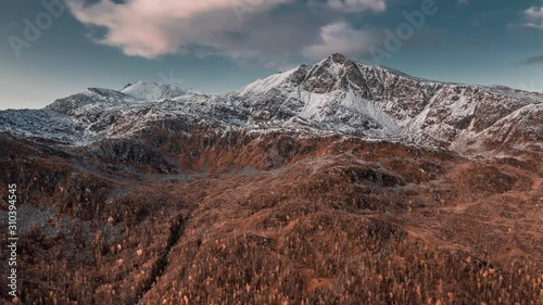 Aerial view of the Kongsviktind mountain on the island of Hinnoya, Lofoten. Autumn Nordic landscape,  fresh snow on the mountain tops, the forest is the color of rust, thin clouds passing above. photo