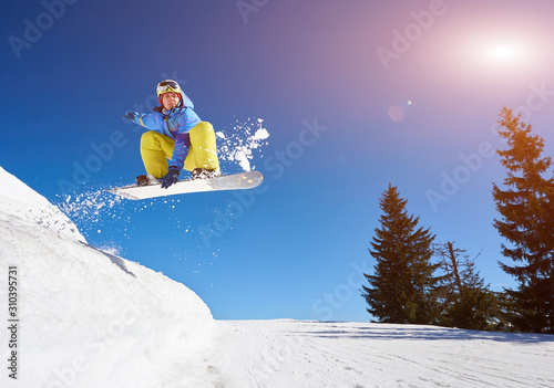 Jumping male snowboarder keeps one hand on the snowboard on blue sky background. Ski season and winter sports concept