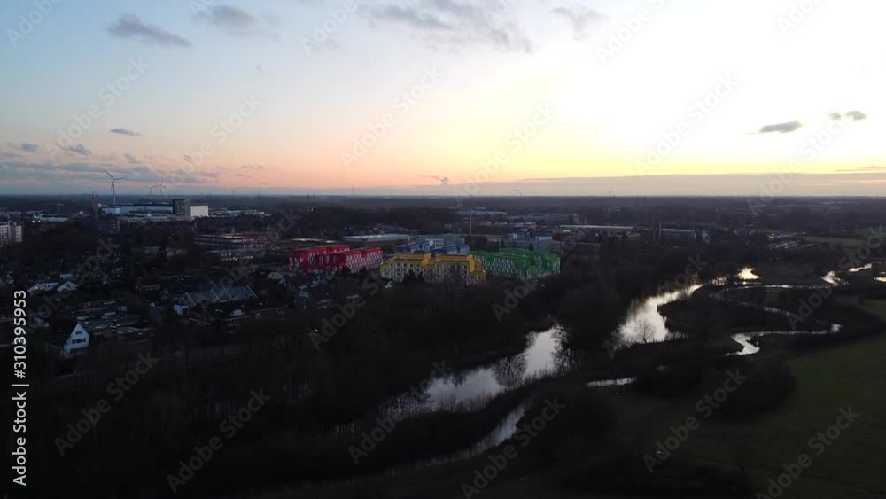 Ascending aerial shot above colorful residential area at horizon during sunset