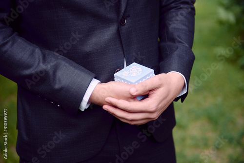 Groom in tuxedo holding blue jewelry gift box with gold wedding rings, copy space. Wedding, Valentine day concept