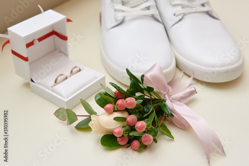 Close up of groom boutonniere with pink ribbon  white male shoes a nd wedding rings on white background  copy space. Modern man accessories. Wedding details