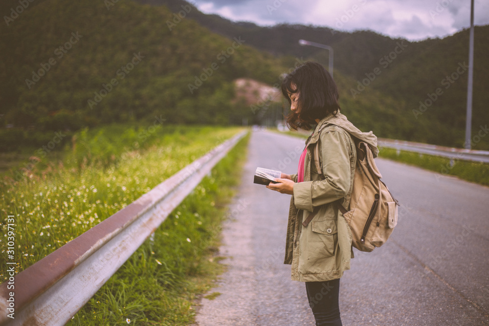 Female backpackers standing on the open road and hold the Bible. The concept goes out to share the gospel. Female backpackers standing on the open road and hold the Bible. The concept goes out to share the gospel.