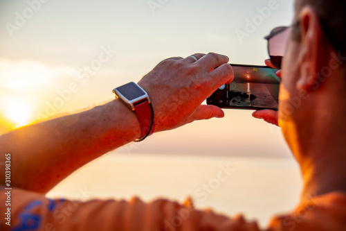 Tourist taking sunset picture with mobile phone at seaside