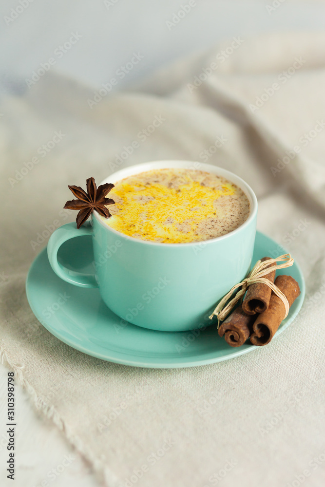 Golden Milk, turmeric latte made with curcuma and other spices: cinnamon, anise. Healthy hot winter drink, natural and organic beverage. Close up, front view. Blue mug, neutral white background Golden Milk, turmeric latte made with curcuma and other spices: cinnamon, anise. Healthy hot winter drink, natural and organic beverage. Close up, front view. Blue mug, neutral white background