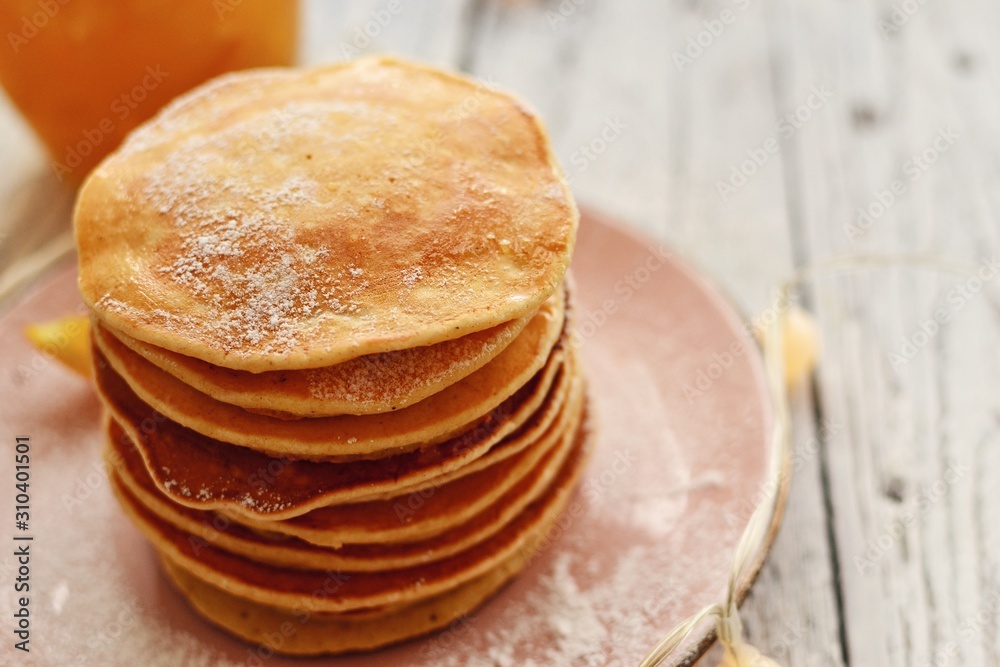 Pancakes with icing sugar and orange. Pancakes in a beautiful pink plate on a light wooden background. Delicious sweet food. Holiday pancakes and Christmas garland on the background. Pancakes with icing sugar and orange. Pancakes in a beautiful pink plate on a light wooden background. Delicious sweet food. Holiday pancakes and Christmas garland on the background.
