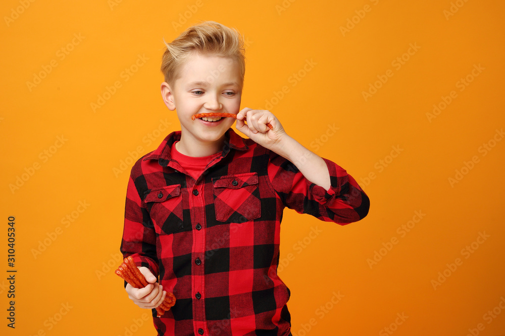 Happy little boy with thin dry pork sausages. Beautiful smiling caucasian boy in the red shirt on the yellow background. Horizontal, straight on.