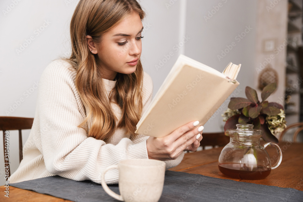 Image of nice caucasian woman reading book and drinking tea Image of nice caucasian woman reading book and drinking tea