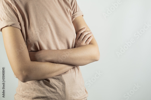 Chest body part of a female person with crossed arms. Woman in simple t-shirt standing in studio background