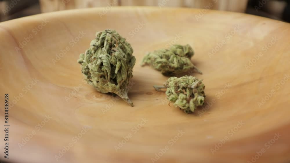 Sativa and indica weed buds in wooden plate on the turning subject table. CBD, THC illustration footage. Full closeup Sativa and indica weed buds in wooden plate on the turning subject table. CBD, THC illustration footage. Full closeup