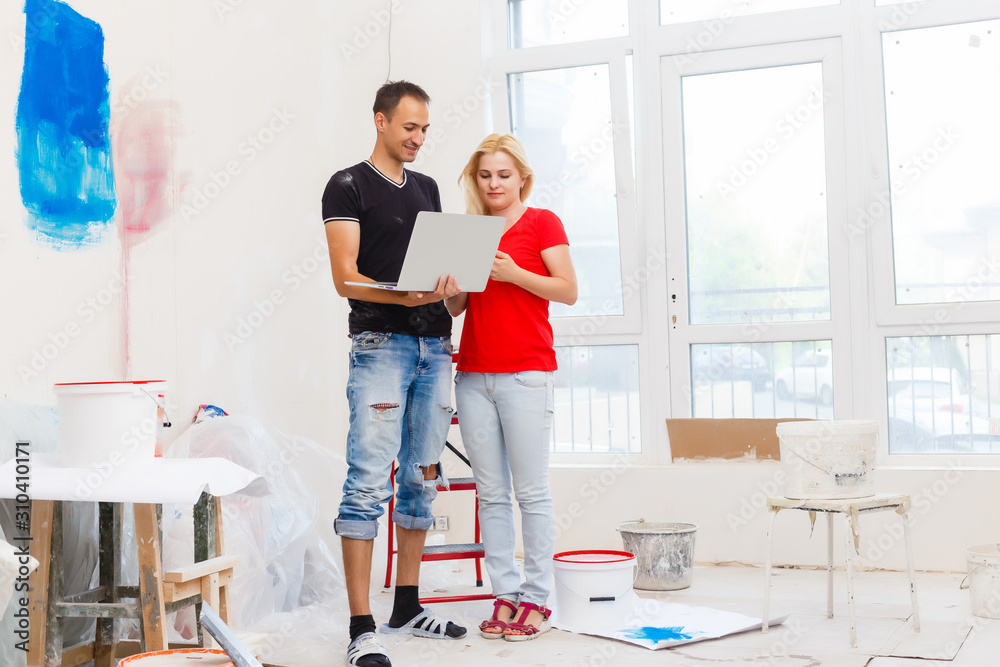 Home makeover and renovation: young couple redecorating their new house and painting walls, the man is leaning on a ladder and posing Home makeover and renovation: young couple redecorating their new house and painting walls, the man is leaning on a ladder and posing