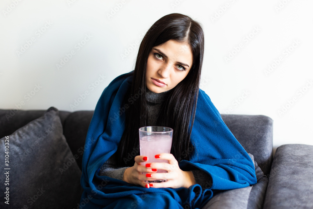 Happy woman holding a white round pill and a glass of water looking at camera sitting on a sofa Happy woman holding a white round pill and a glass of water looking at camera sitting on a sofa