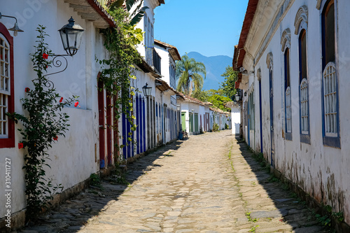 Fototapeta Naklejka Na Ścianę i Meble -  View to mountain through a typical cobblestone street with colonial buildings in the late afternoon sun in historic town Paraty, Brazil