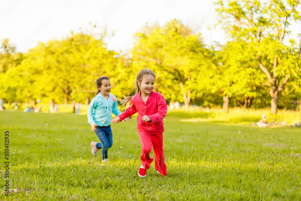 Fototapeta premium Children run on the green grass holding hands. Girls running around the lawn with grass playing with splashes of water to water plants.