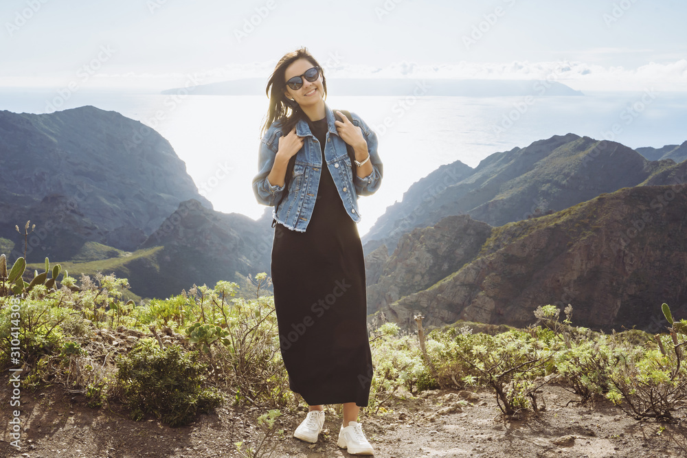 Happy woman with backpack on the background of the ocean and mountains. Travel and lifestyle concept.