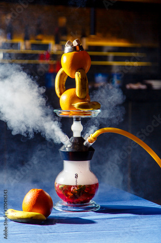 Hookah on oranges and bananas. Citrus hookah. Hookah with round clear bulb with a red liquor. A bowl of hookah made of oranges, in which bananas are inserted.  photo