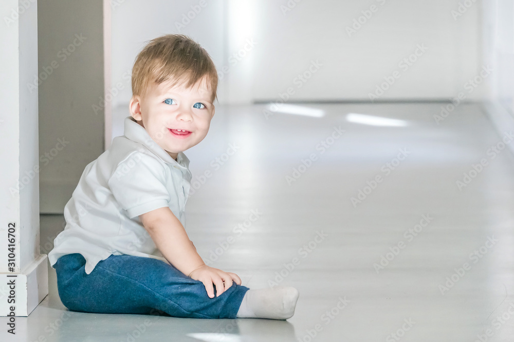 Smiling blue-eyed baby sitting on the floor.