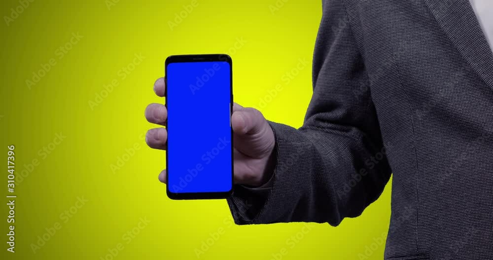 man in a suit holding smartphone into the camera with blue croma key on yellow background man in a suit holding smartphone into the camera with blue croma key on yellow background
