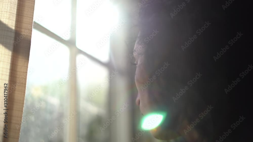 Young attractive woman looking out the window on a bright day with shunshine coming in the window - focus pull from woman to window - melancholy mood