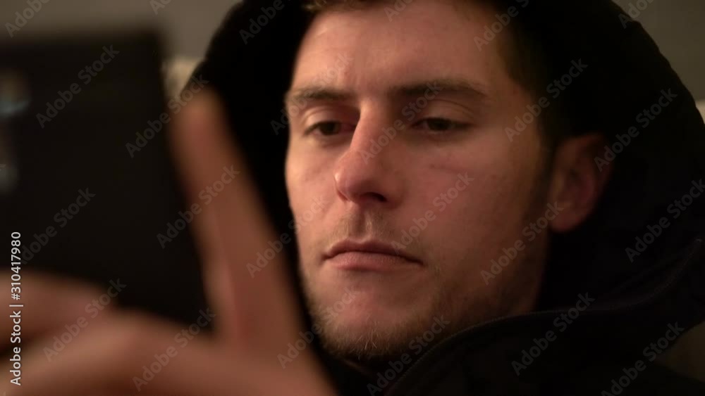 Young man relaxing and reading on a smartphone or tablet - emphasis on face and concentration Young man relaxing and reading on a smartphone or tablet - emphasis on face and concentration