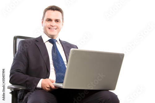 A smiling businessman holds a laptop while sitting in a chair. Close-up.