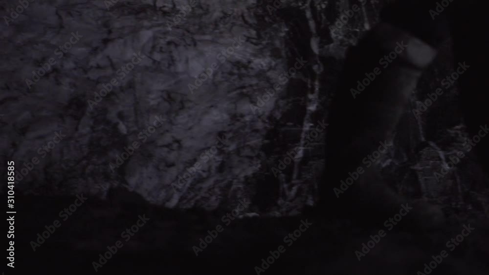 Close up of person in gumboots walking in a dark underground gold mine Close up of person in gumboots walking in a dark underground gold mine