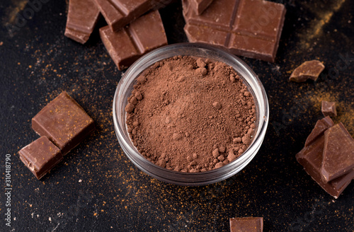 Cocoa powder in a plate on a black background next to chocolate. close-up