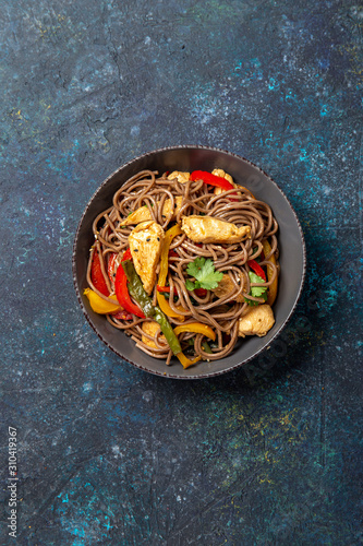 Japanese dish buckwheat soba noodles with chicken and vegetables carrot, bell pepper and green beans in grey bowl, top view, copy space